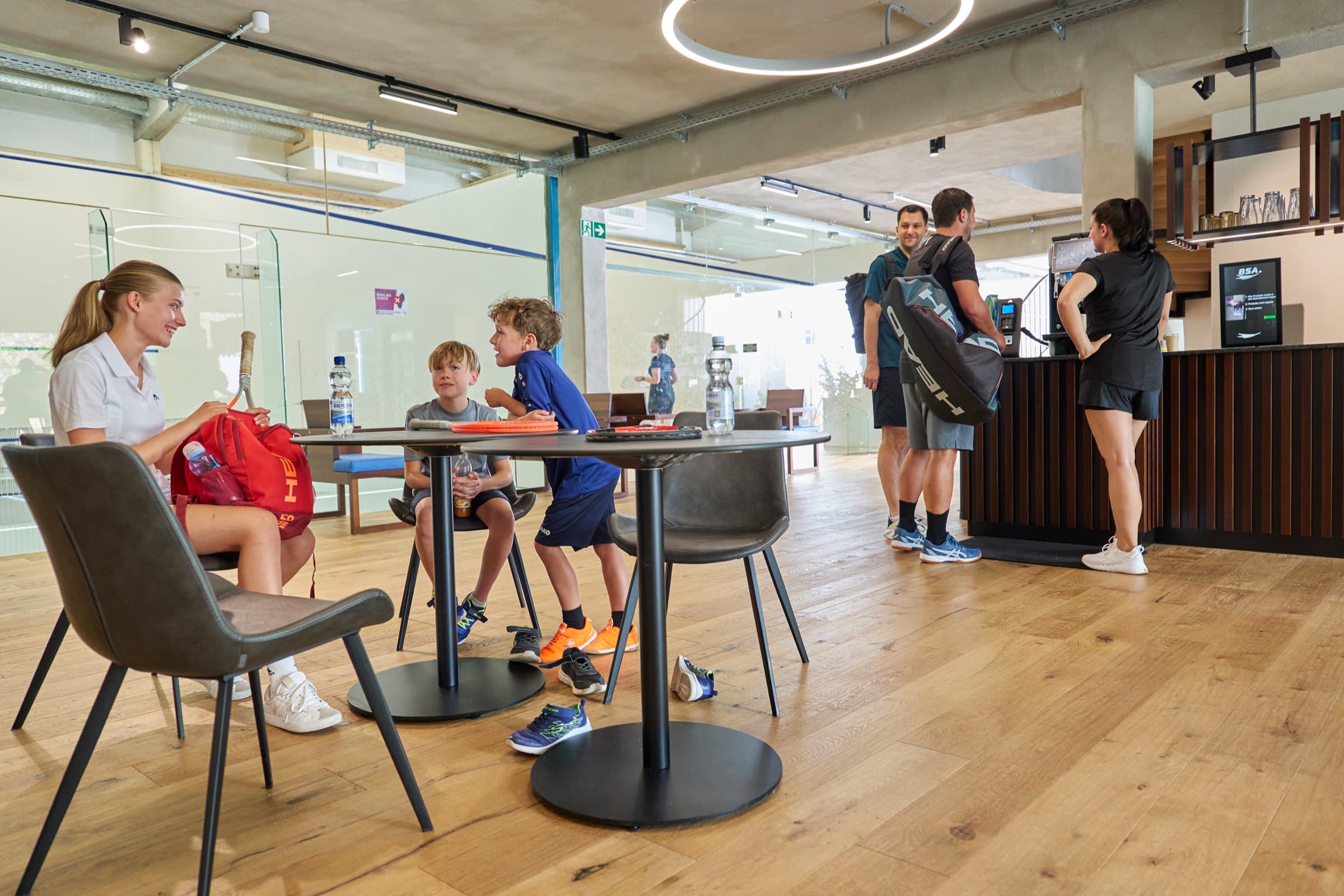 Familien und Gäste im Bistro der Ballsport Arena Schwaben — im Hintergrund die Squash-Courts und der Empfang.