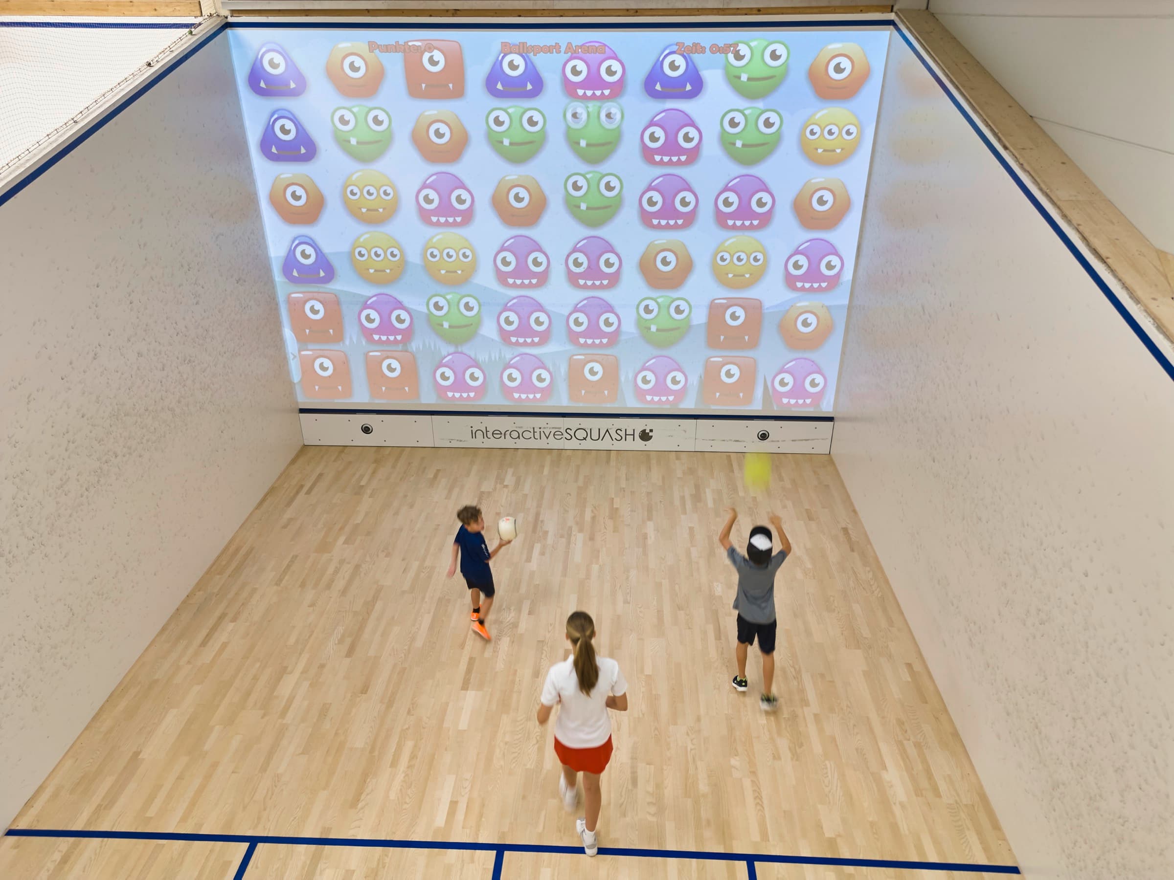Kinder spielen vor der leuchtenden Interactive-Squash-Wand.